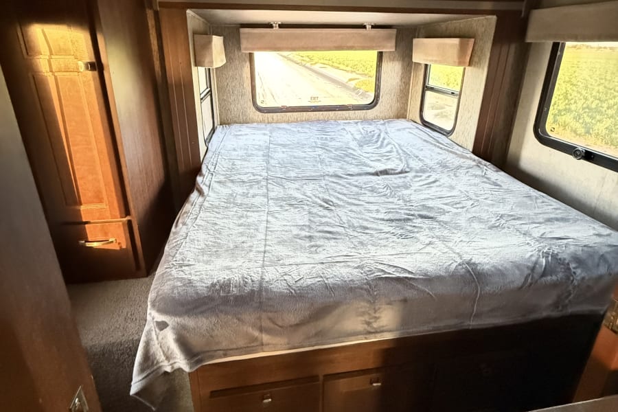 Inside an RV rental: a bright bedroom features a large bed, built-in storage, and scenic window views.
