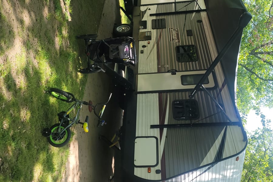 Anniversary camping getaway with our Coleman RV rental! Features a spacious awning, bike, and fire pit at the campsite.
