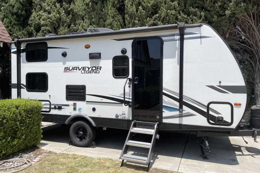 This white Surveyor Legend travel trailer with extended steps is ideal for an RV rental. It's parked on concrete.