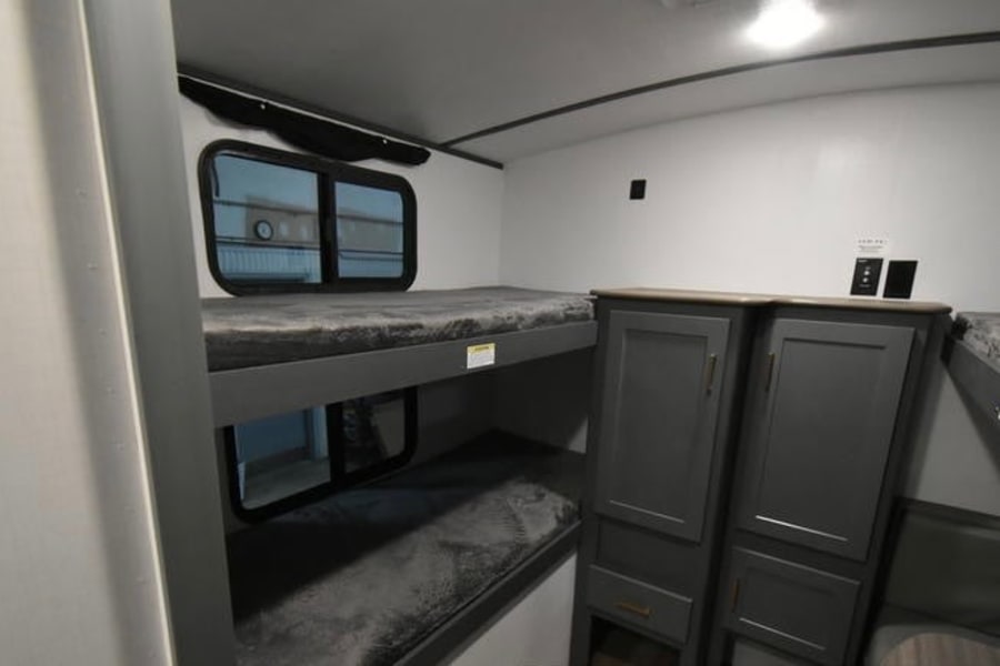 Modern RV rental interior featuring dark gray bunk beds with windows, alongside gray cabinets, providing comfortable sleeping arrangements.