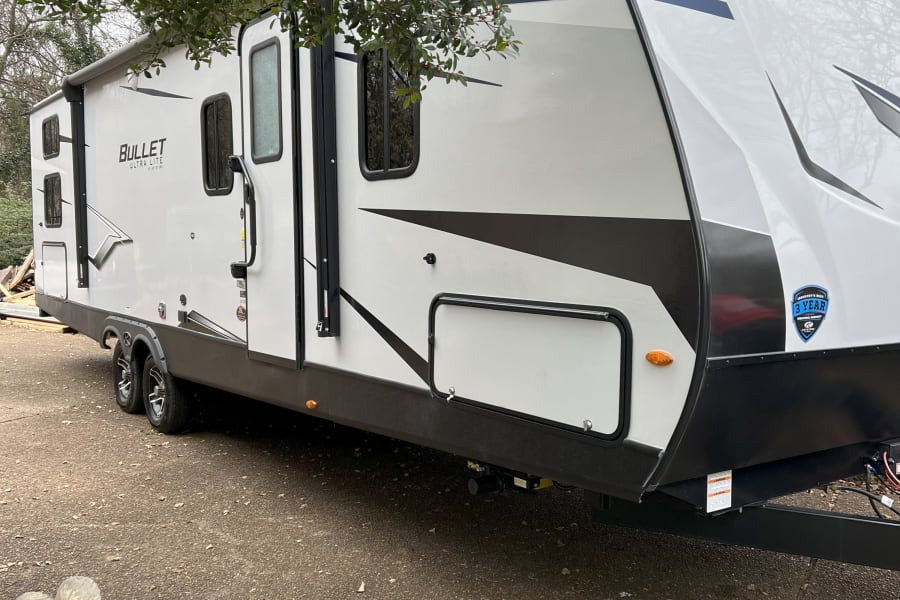 A modern, white Bullet Ultra Lite travel trailer RV rental with black accents is parked on a driveway.