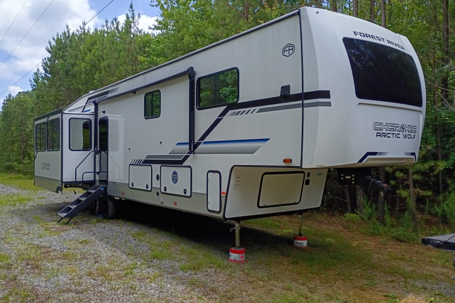 A large white fifth-wheel RV rental, a Forest River Cherokee Arctic Wolf, parked on gravel, set up for camping.