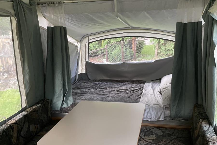Pop-up camper interior with dining area, bed, and small kitchen sink, ideal for an RV rental.
