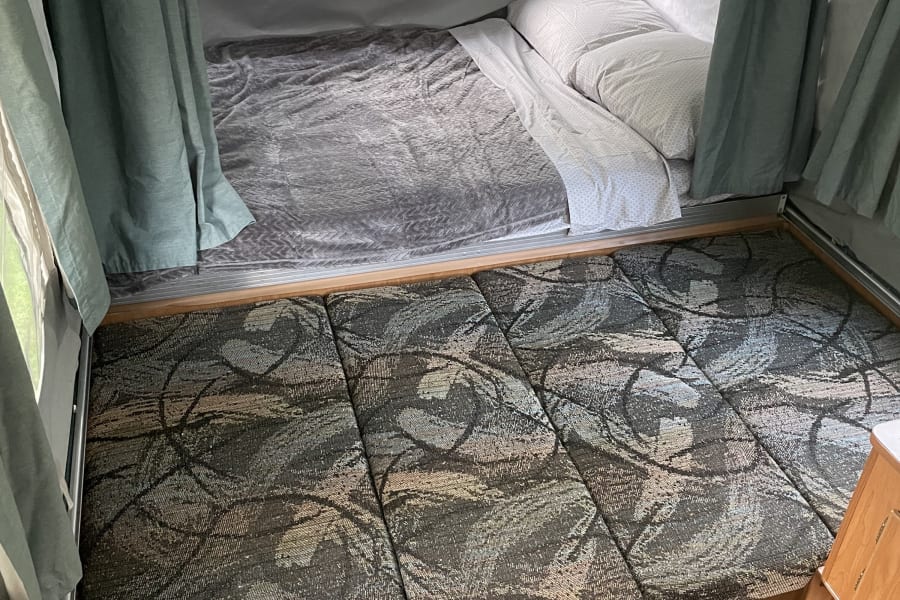 View inside an RV rental showing a comfortable bed, patterned cushions, and green privacy curtains.