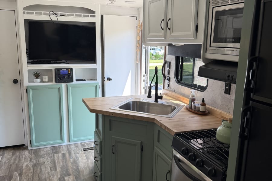 Refurbished rv rental interior featuring a modern kitchen with mint green cabinets, wood counters, and a cozy TV living space.