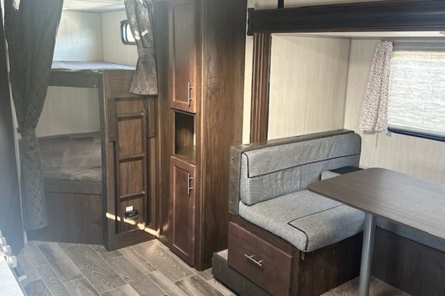 Cozy rv rental interior featuring bunk beds with privacy curtains, a storage cabinet, and a dinette for eating/lounging.
