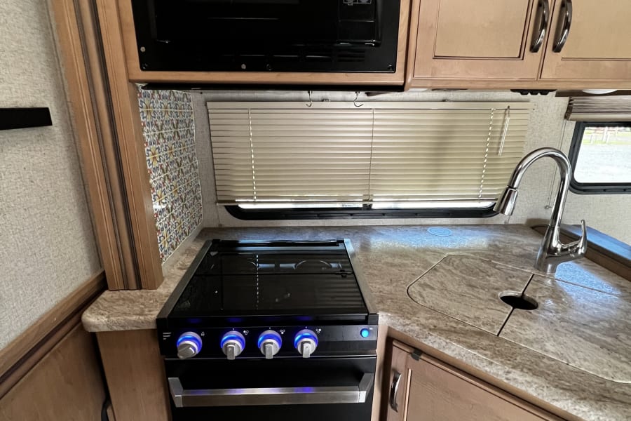 This modern RV rental kitchen features a microwave, gas range, sink, and light wood cabinetry, showcasing efficient design.