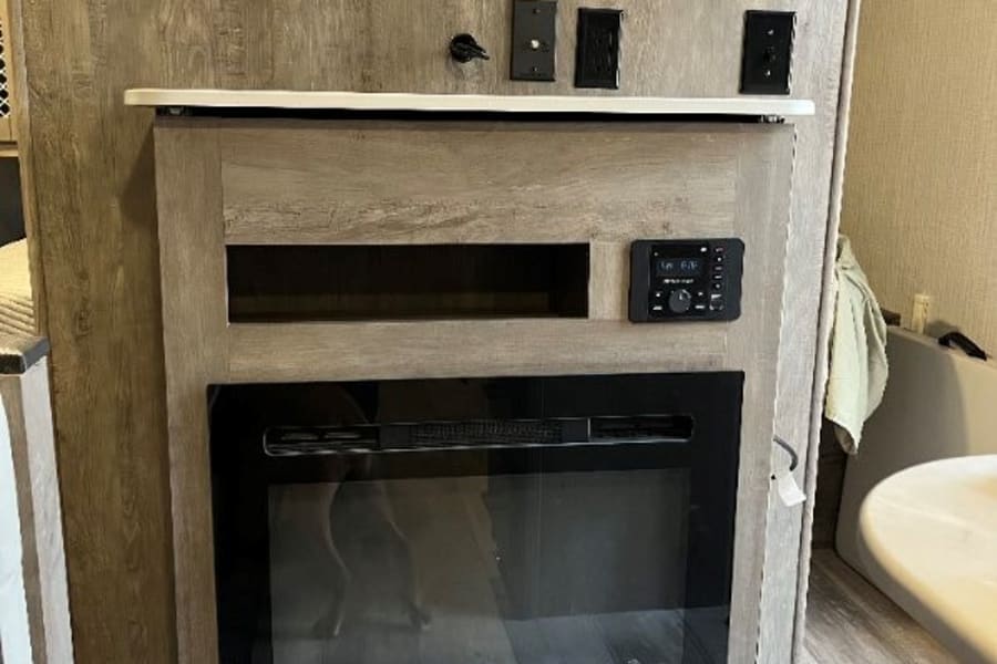 RV rental living area with a modern electric fireplace, open shelf, and controls, offering cozy comfort.
