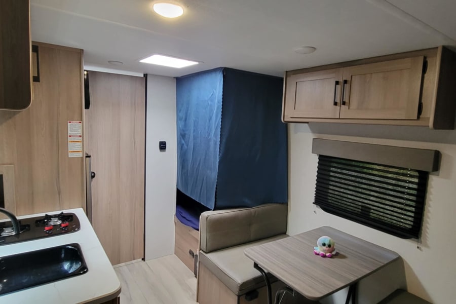 Inside a modern RV rental: a compact kitchen, dining booth, and private sleeping nook for travel.