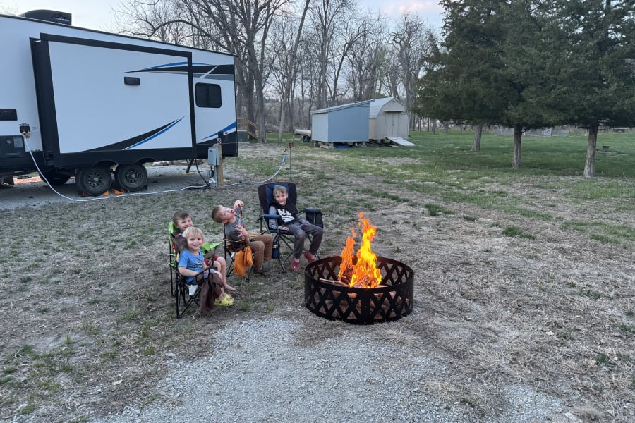 Family RV rental trip: Boys relax by a warm campfire next to their parked travel trailer.