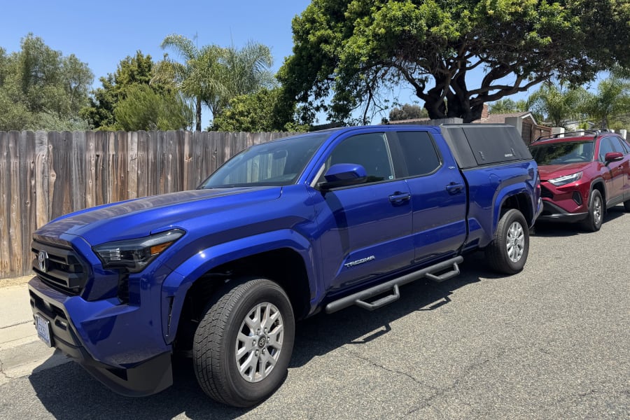 A blue Toyota Tacoma pickup with bed cap & red RAV4 parked. Adventure awaits! Look into rv rental options.