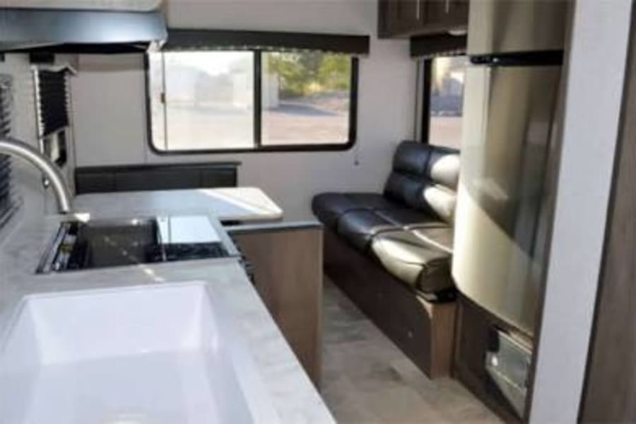 Inside this RV rental: a modern kitchen with white sink, a dining area, and a black leather sofa next to a fridge.