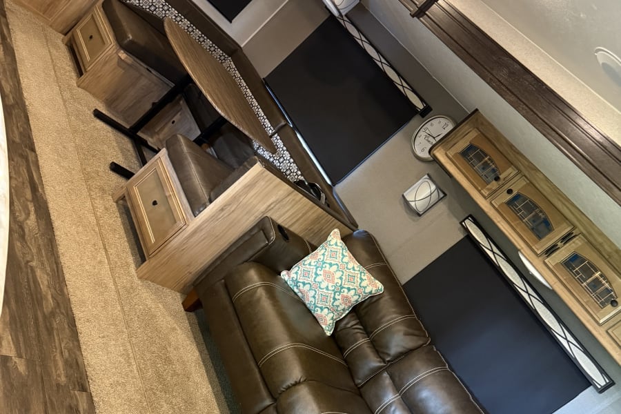 Explore this RV rental interior: cozy brown sofa, dining area, and abundant wood cabinetry. A welcoming mobile living space.