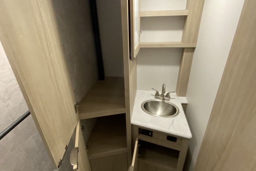 Compact RV rental bathroom with sink, toilet, and ample storage cabinets/closet for comfortable travel.