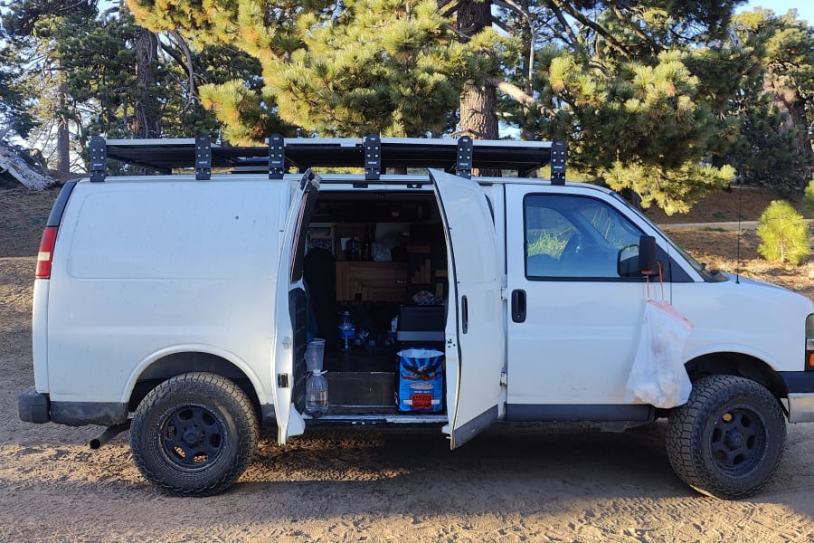 White camper van parked in a pine forest with open side door. See inside this RV rental ready for adventure!