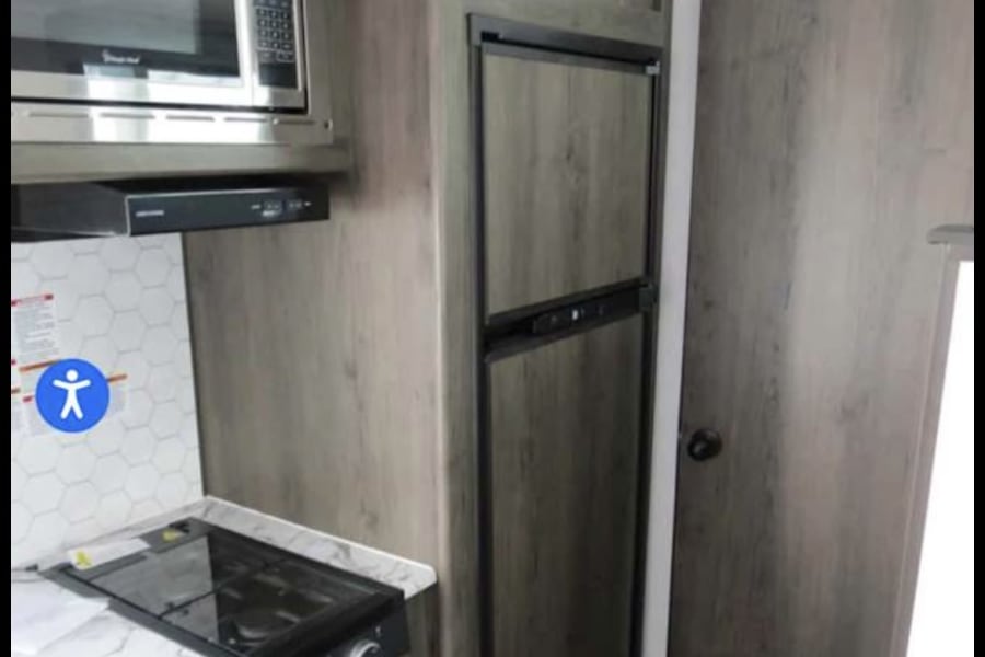 This RV rental kitchen features a microwave, refrigerator, and cooktop integrated into sleek, light wood-look cabinets.