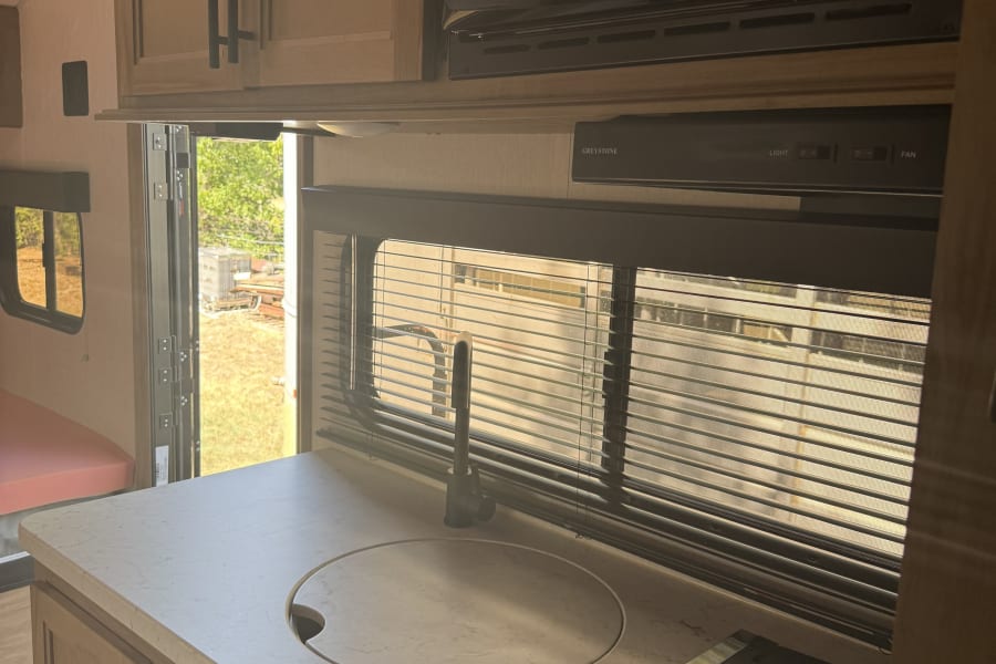 This RV rental features a compact kitchen with a microwave, sink, and stove, perfect for your next camping adventure.