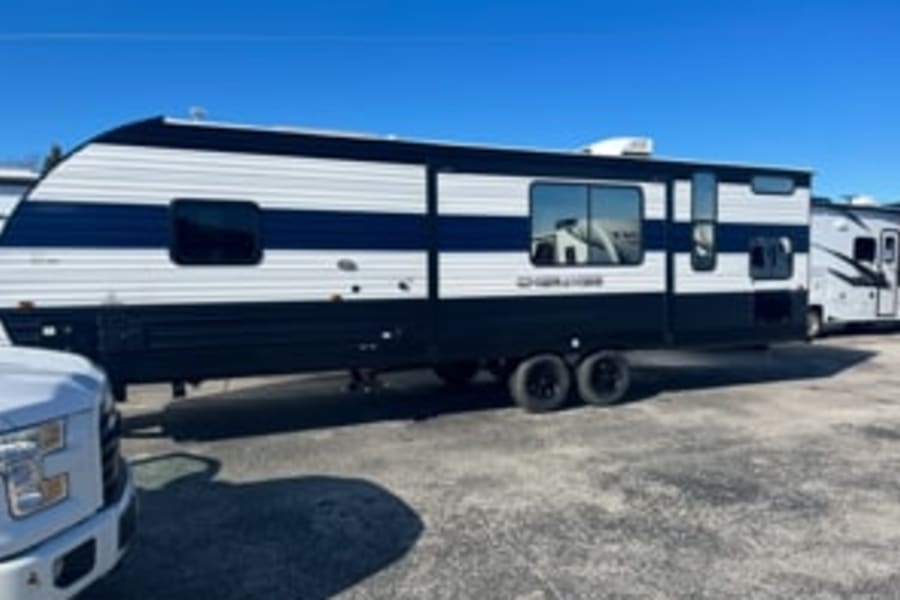 Ready for adventure? This large, white & navy striped RV rental is parked on asphalt under a clear sky.