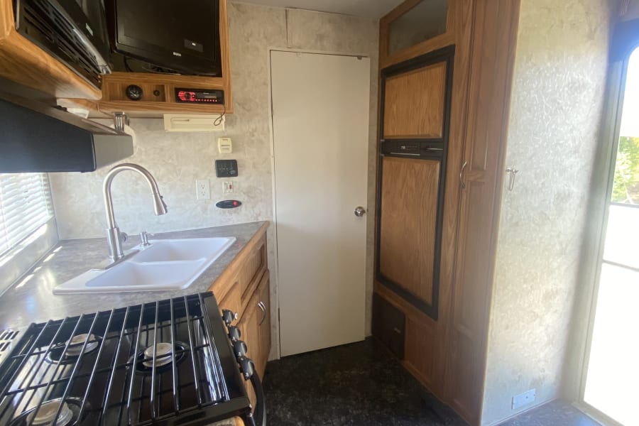 Experience home comfort in this RV rental kitchen, equipped with a gas stove, sink, microwave, and fridge for your adventures.