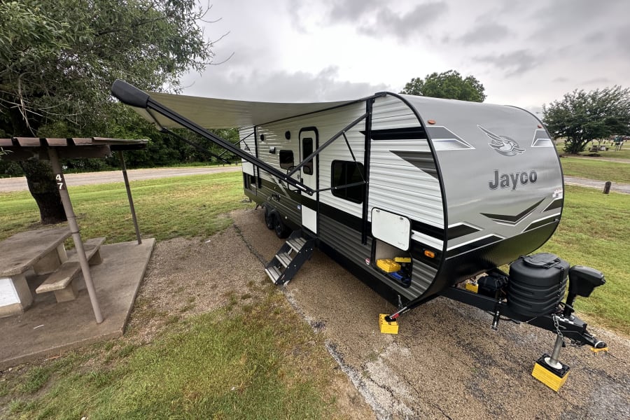 Grey Jayco travel trailer at a cloudy campsite, ready for an RV rental adventure. Awning extended, with a picnic table.