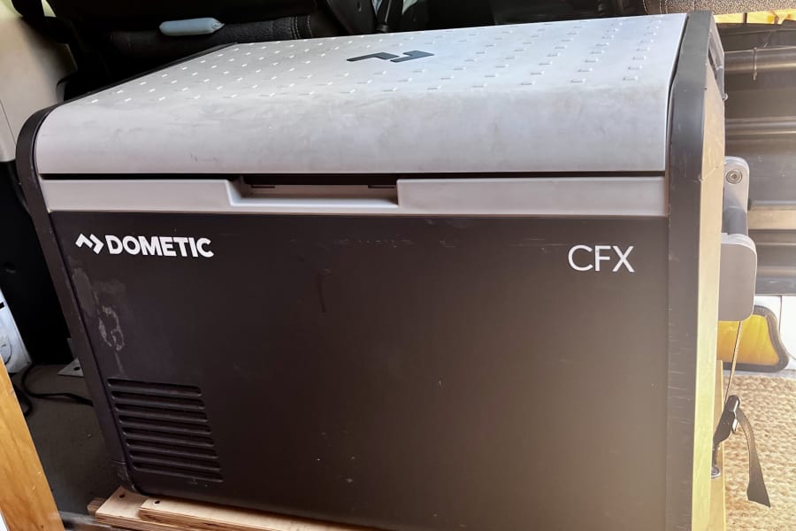 A Dometic CFX portable fridge, on a slide-out tray, ready for your rv rental trips. Seen in a camper van interior.