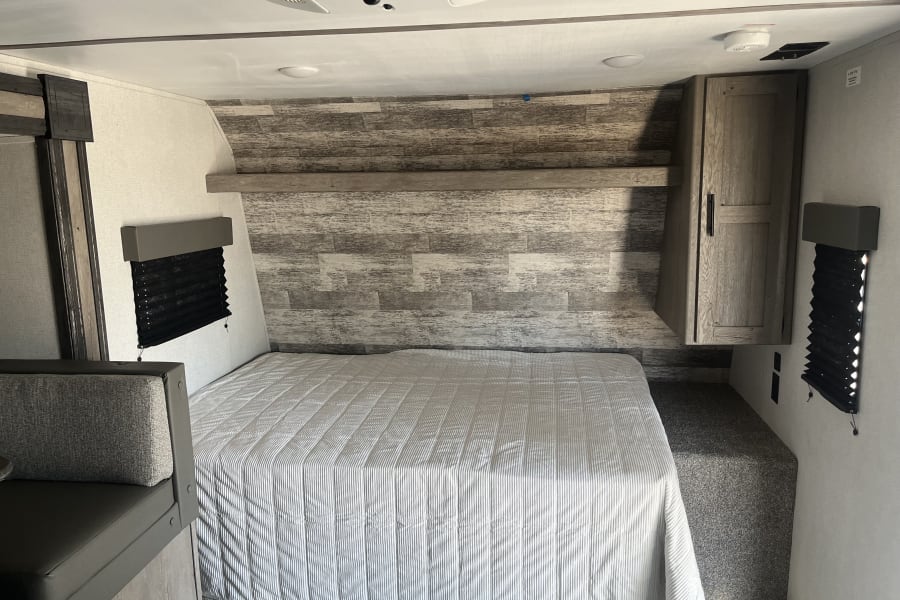 Comfortable RV rental bedroom featuring a striped bed, rustic wood accent wall, built-in cabinet, and practical design.