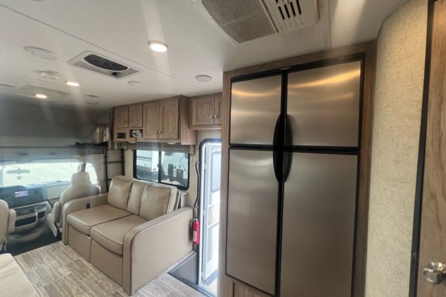 RV rental interior: A bright living area featuring a comfortable sofa, kitchen cabinets, and a large stainless steel refrigerator.