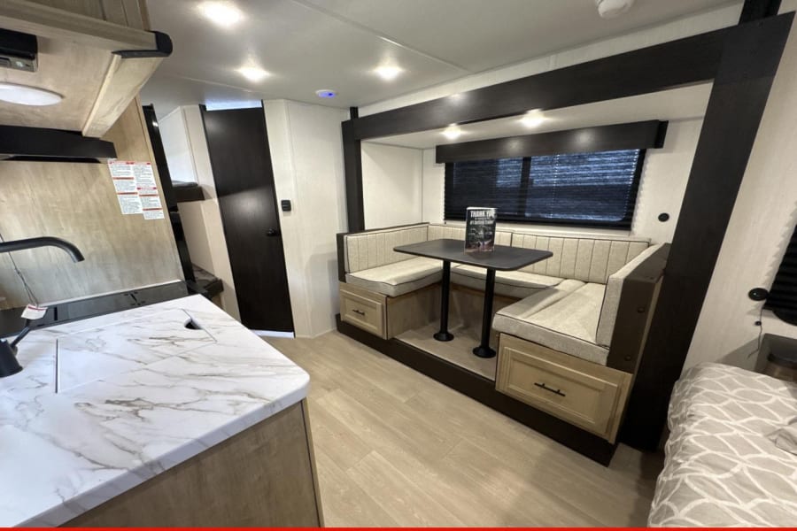 RV rental interior featuring a compact kitchen, dining booth, and bed area, designed for travel comfort.