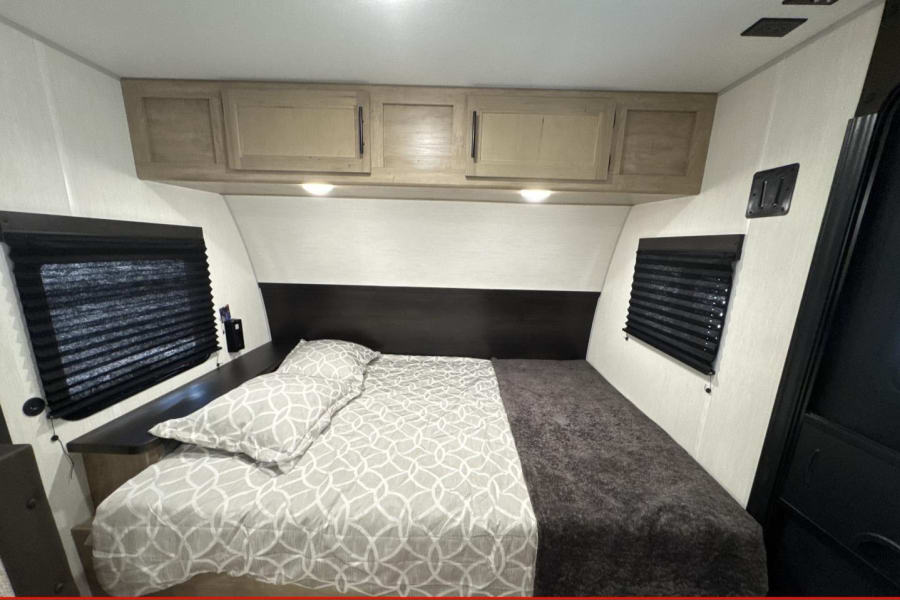 RV rental bedroom featuring a large bed, overhead storage, and dual windows with blinds.