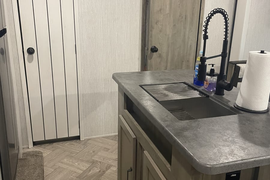 Modern RV rental interior featuring a kitchen island with sink, black faucet, pendant light, and "Life's an Adventure" sign.