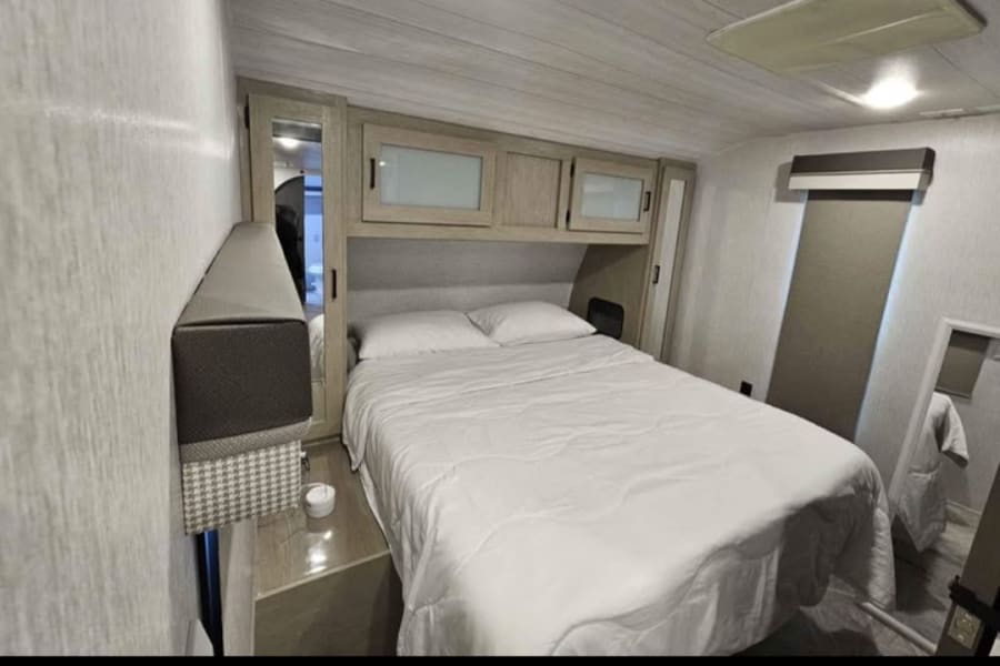 Cozy RV rental bedroom featuring a queen bed, overhead storage, and a full-length mirror for your travels.