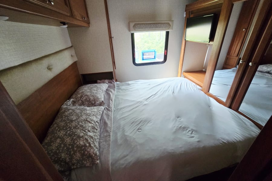 A clean, inviting bedroom with a made bed inside an RV rental. Features a window and mirrored closet.