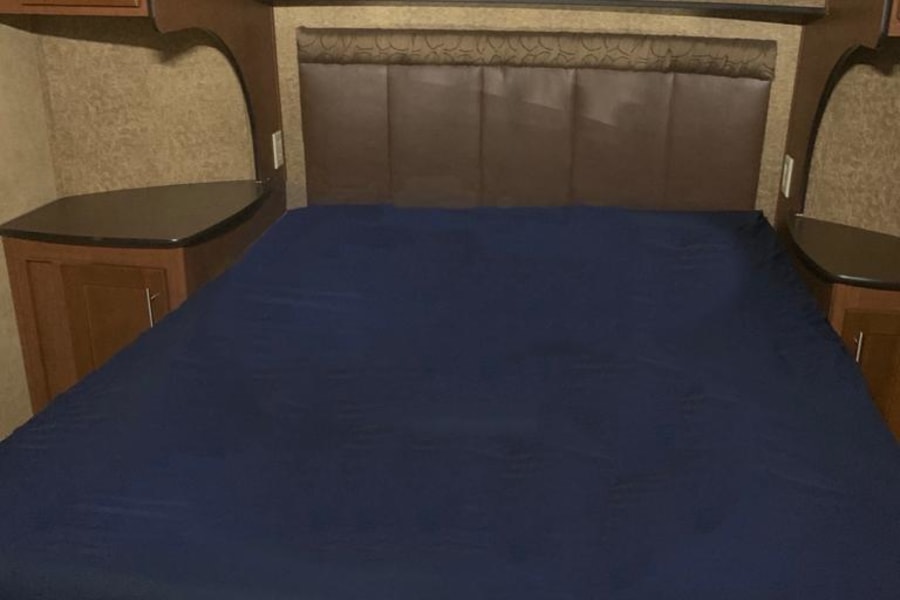 Cozy RV rental bedroom featuring a large bed with blue sheets, brown headboard, and built-in wood cabinets for comfort.