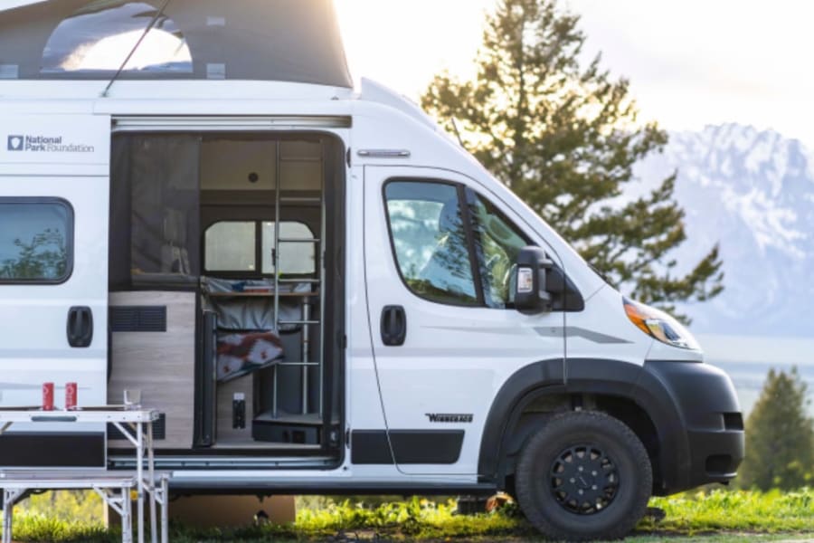 White camper van RV rental (National Park Foundation edition), pop-top open, in a breathtaking mountain landscape.
