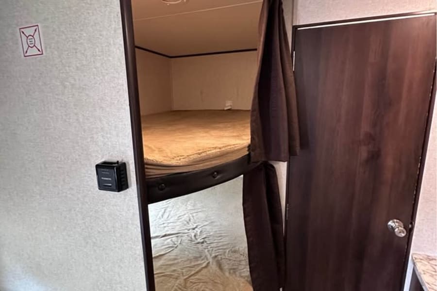 This RV rental features two cozy bunk beds with privacy curtains, a nearby door, and comfortable seating, ideal for family trips.