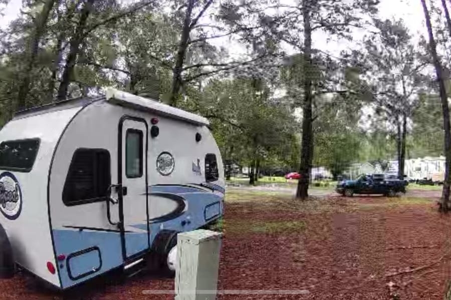 Experience nature with an RV rental! A compact R-Pod travel trailer is parked at a wooded campsite, ready for your next adventure.
