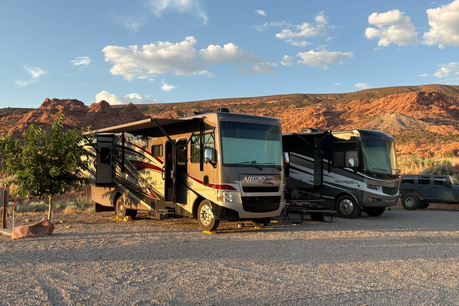 Two RV rental motorhomes, a tan Allegro and grey Georgetown XL, with awnings out,