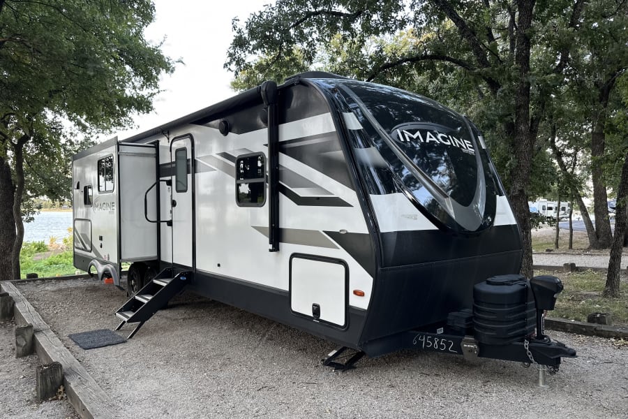 Spacious Imagine RV rental parked at a serene lakeside campground, with its slide-out extended and steps down.
