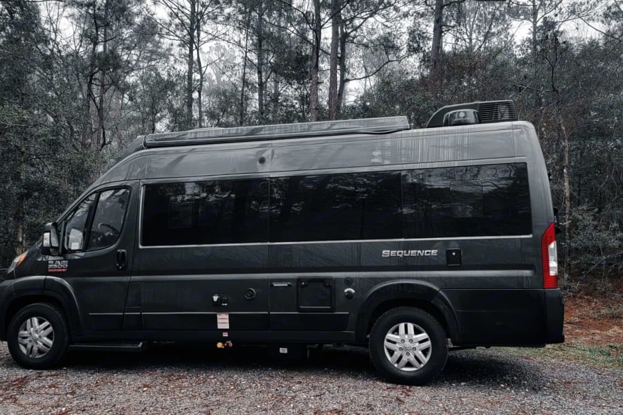 Dark grey Thor Sequence camper van, ideal for an rv rental adventure, parked on a gravel road by a dense, muted forest.