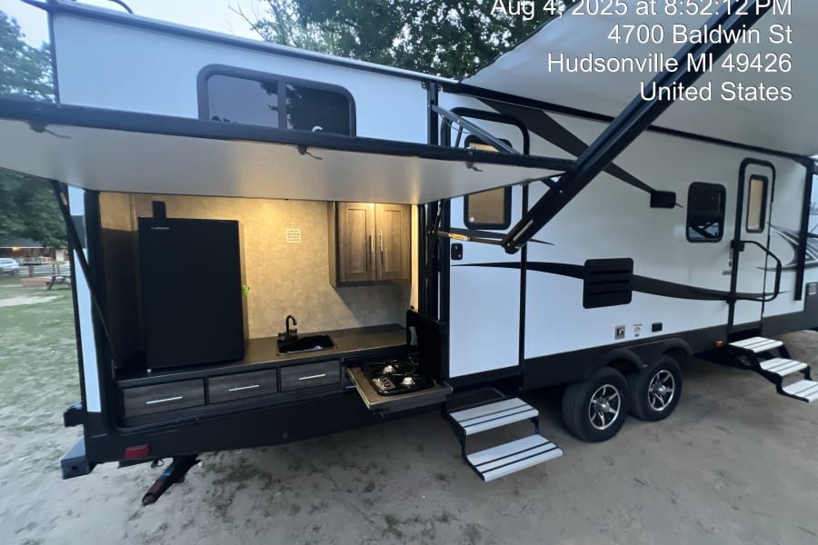 This RV rental showcases an outdoor kitchen with a fridge, sink, and stove, perfect for camping adventures.