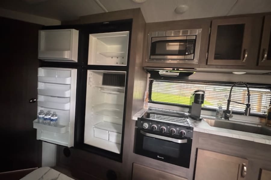 Inside an RV rental, a modern kitchen features an open fridge, microwave, stovetop, oven, and sink with a coffee maker.