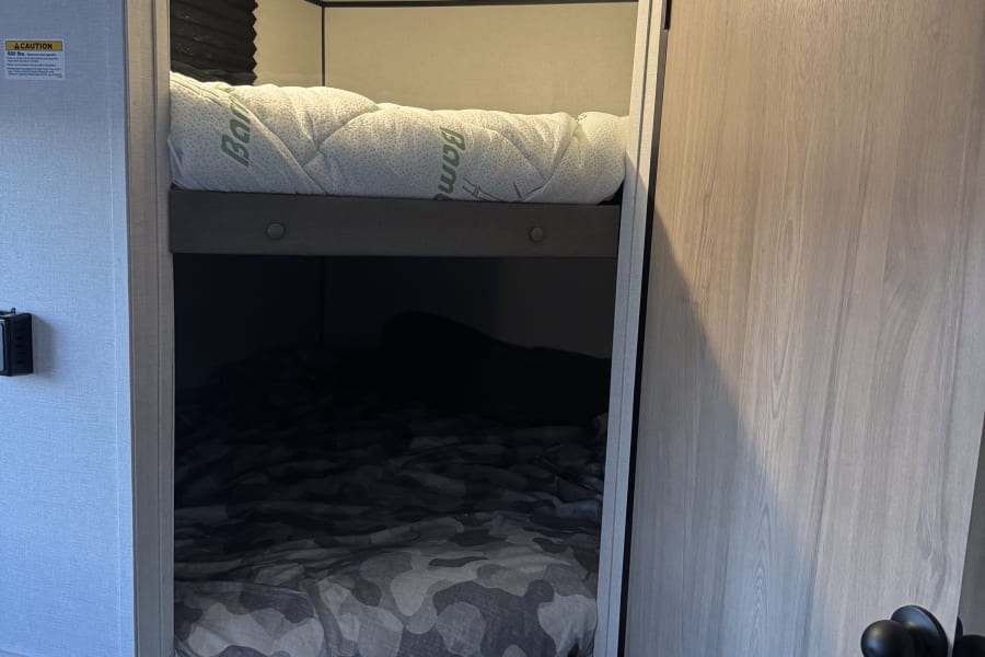 RV rental bunk beds: View of a compact sleeping area with a quilted top mattress and a camo-patterned lower bed.