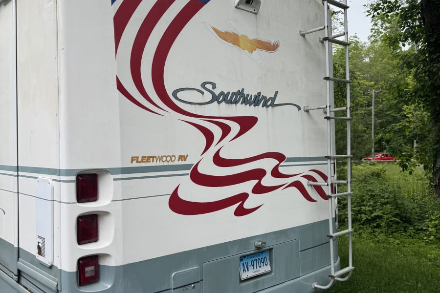 Rear of a Fleetwood Southwind RV, featuring a patriotic flag decal and ladder. This RV rental is parked in a green, wooded setting.