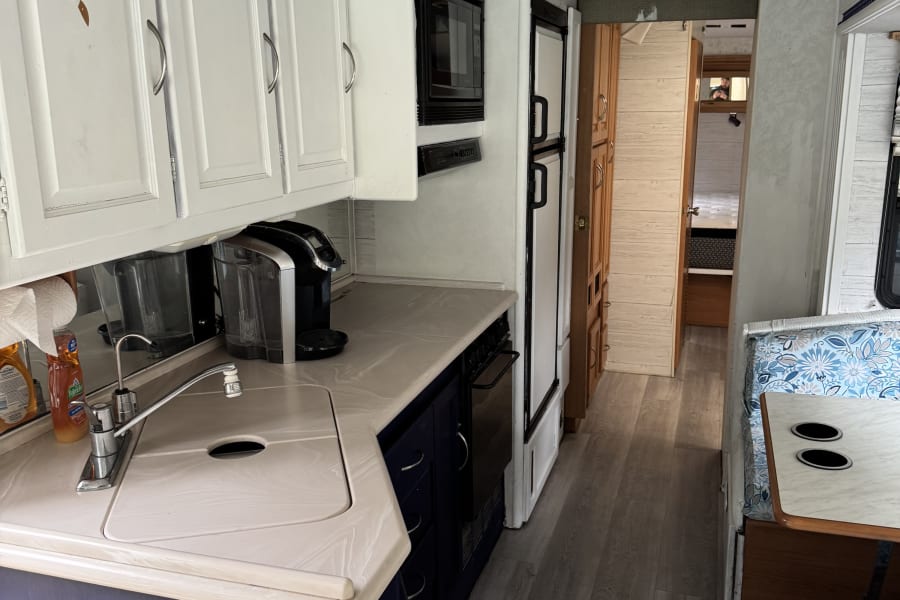 Renovated RV rental interior features a functional kitchen with sink, microwave, and dining nook. Modern flooring & bright cabinets.