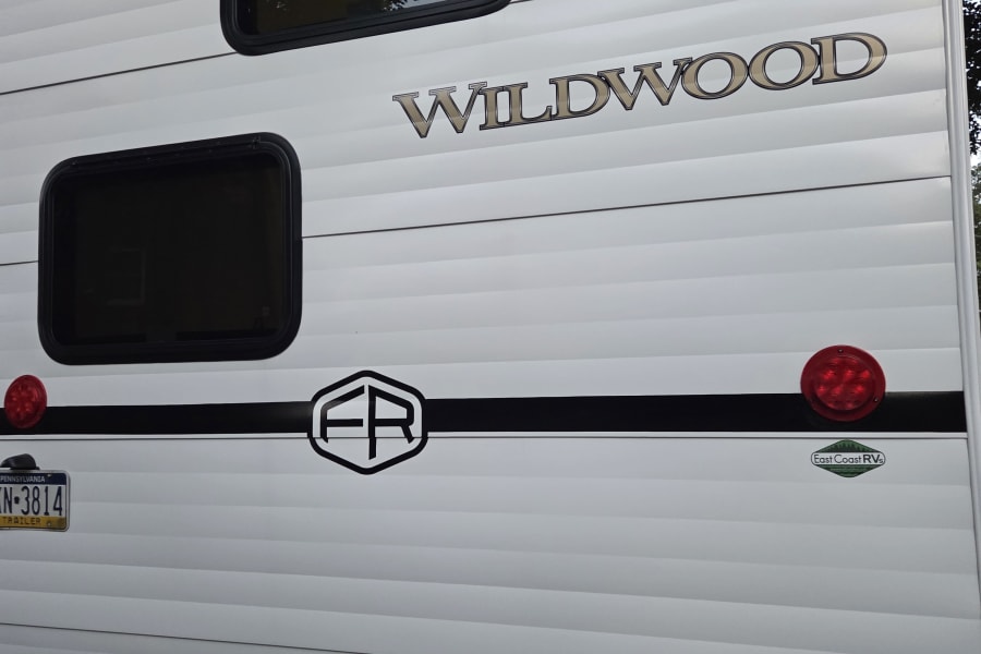 Rear of a white Wildwood RV rental: features include windows, red tail lights, a black stripe, and a PA trailer plate.