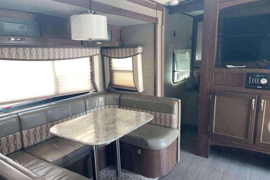 Spacious RV rental interior featuring a comfortable dining booth, entertainment center, and modern finishes.