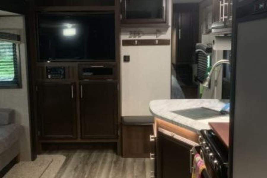 Explore this RV rental's inviting interior: A comfy living area with TV on the left, modern kitchen with sink on the right. Dark wood decor.