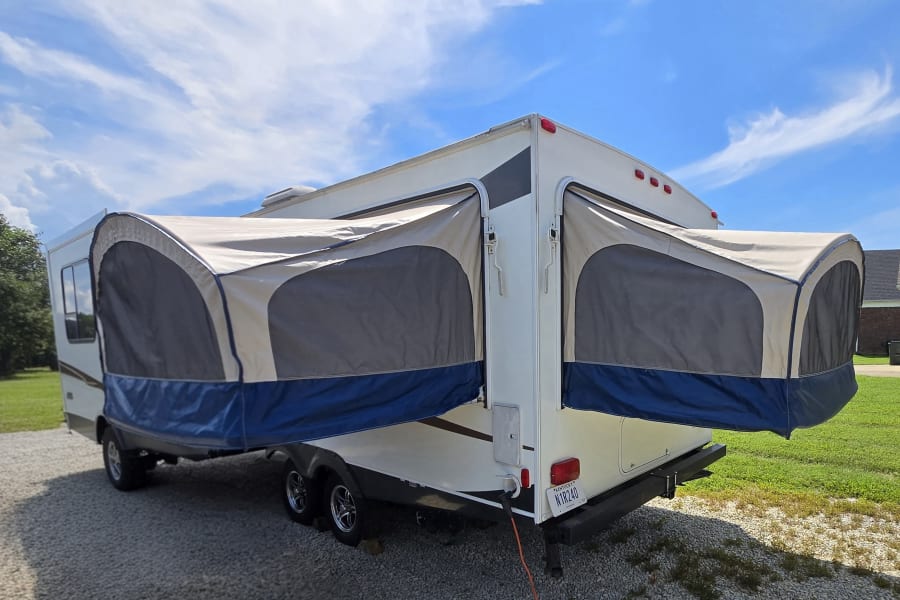 RV rental: Parked white hybrid camper with tan/blue pop-out bunks on gravel driveway. Kentucky plate visible.