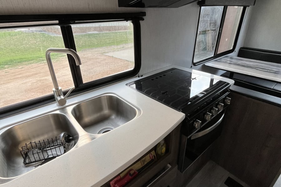 Modern RV rental kitchen: double sink, gas range, microwave, and dinette. Ready for your road trip adventures!