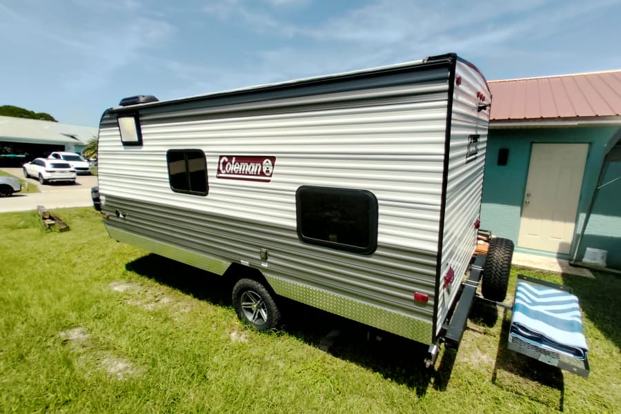 This Coleman RV rental is parked on grass, featuring windows and a rear-mounted spare tire.